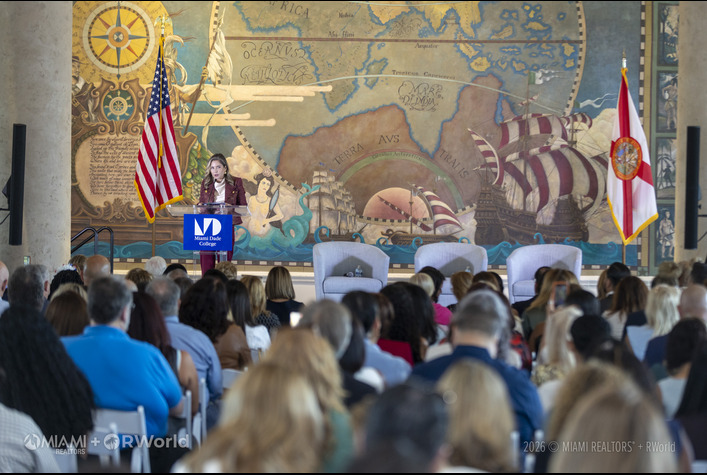 MIAMI REALTORS® + RWorld Residential President Dinorah Guerra speaking in front of the New World Mural 1513, a monumental 44-foot by 20-foot historical painting inside the Grand Hall of the Freedom Tower in Miami.